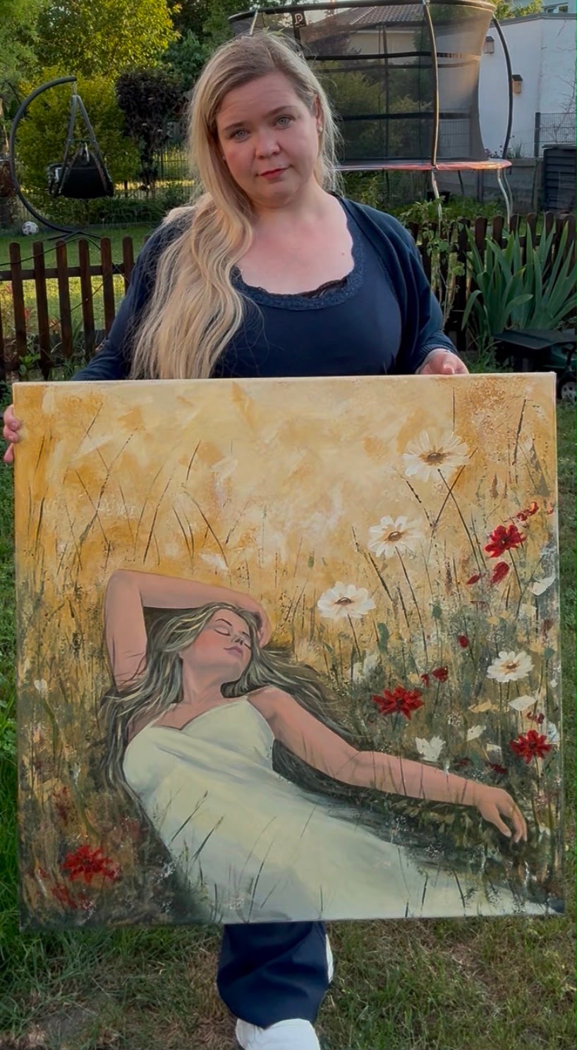 Kathrin Caglar mit einem ihrer Werke — eine Frau, die in einer Blumenwiese liegt
